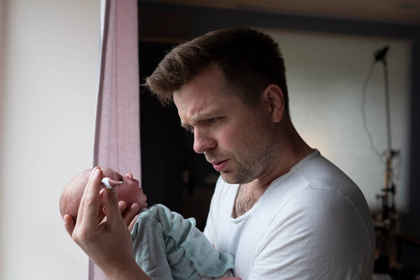 Preoccupato per il padre che guarda il termometro che tiene in mano il suo neonato. - Foto, immagini