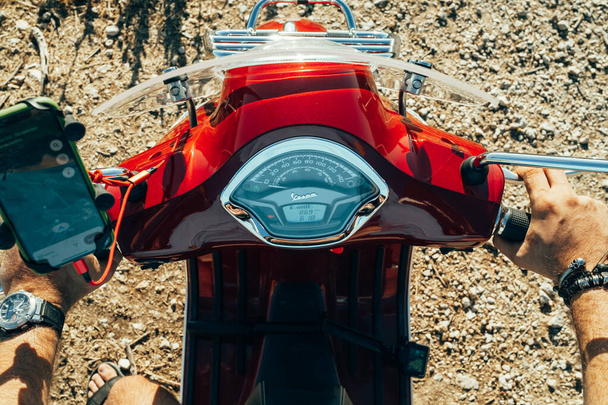 Corfu, Greece - September 2021. Mans hands on steering wheel of red Vespa, guy driving moped or scooter, close-up view. Driver rides motor bike. Handlebars of motorcycle. - Φωτογραφία, εικόνα