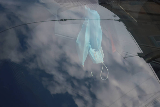 máscaras médicas penduradas no espelho retrovisor atrás do pára-brisas do carro, que reflete o céu - Foto, Imagem