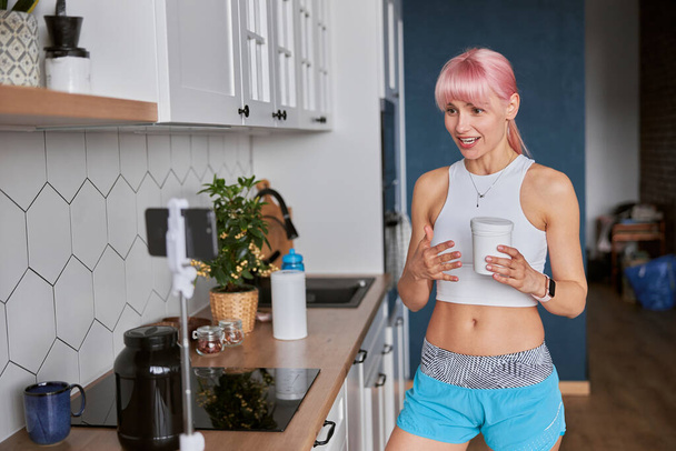 Mujer joven muestra frasco de suplemento dietético de grabación de vídeo nuevo en la cocina - Foto, imagen