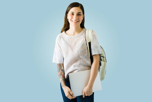 笑顔の若い女性は彼女のラップトップとバックパックを運ぶ。ラテン系の大学生が学校に戻る - 写真・画像
