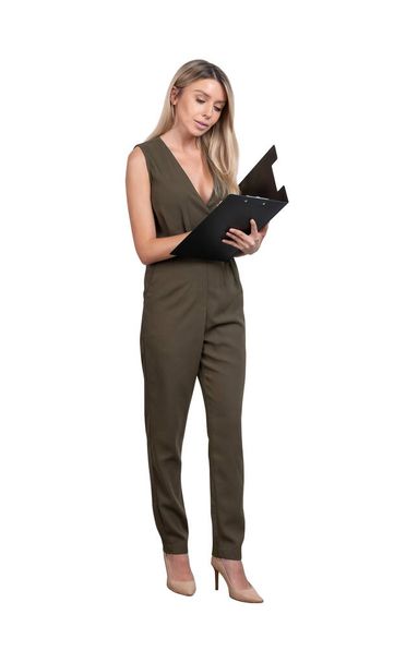 Young attractive businesswoman wearing green dress is standing and holding clipboard. Concept of contemporary successful business people. Isolated over white background - Photo, Image