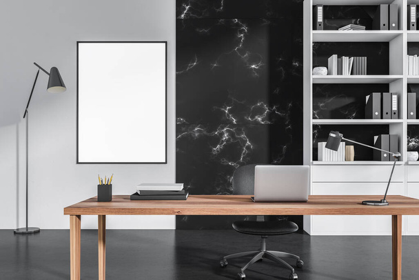 Dark office interior with white empty poster, laptop, comfortable armchair, desk, books, folders, bookshelf and concrete floor. Perfect place for working process. Minimalist design. 3d rendering - 写真・画像