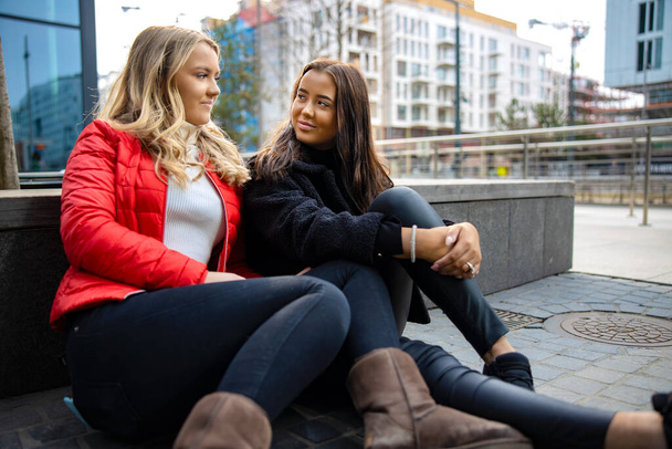 Portret van twee lachende vrouwelijke vrienden die naar elkaar kijken in de stad - Foto, afbeelding