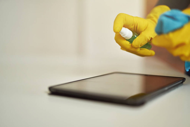 Primer plano de la señora de la limpieza en guantes de goma usando spray antibacteriano desinfectante y tela mientras se desinfecta la pantalla de la tableta digital PC - Foto, Imagen
