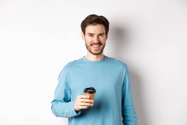 Iloinen mies juo kahvia kahvilasta take-away ja hymyilee, seisoo paperimuki valkoisella taustalla - Valokuva, kuva