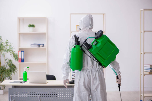 Contratista masculino joven desinfectando oficina durante pandemia - Foto, imagen