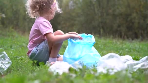 маленька дівчинка видаляє пластикове сміття і кладе його в біорозкладаний мішок для сміття на відкритому повітрі. Концепція екології, переробки відходів та охорони природи. Захист навколишнього середовища
 - Кадри, відео