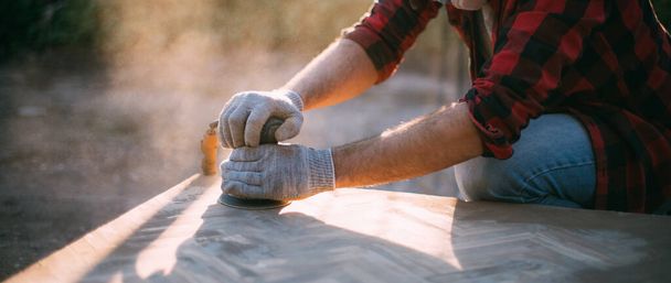 A male carpenter works with a wood grinder. Professional equipment and protective equipment. Young professional sanding wood table top outdoors. - Foto, immagini
