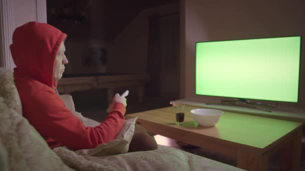 Man in the hood watches TV , sits on the couch at home in the evening, chromakey - Footage, Video