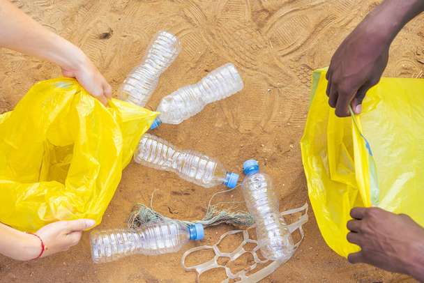 Ręce zbierały odpady plastikowych butelek na plaży, śmieci są na plaży. Wolontariusze zbierający śmieci na plaży. Koncepcja ekologiczna. - Zdjęcie, obraz