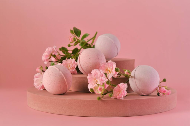 Bath bombs with rose extract.Pink bath bombs and pink rose flowers on burgundy pedestal on a pink background.Organic cosmetics. natural cosmetics with rose extract.Flower Bath Bombs - Fotoğraf, Görsel