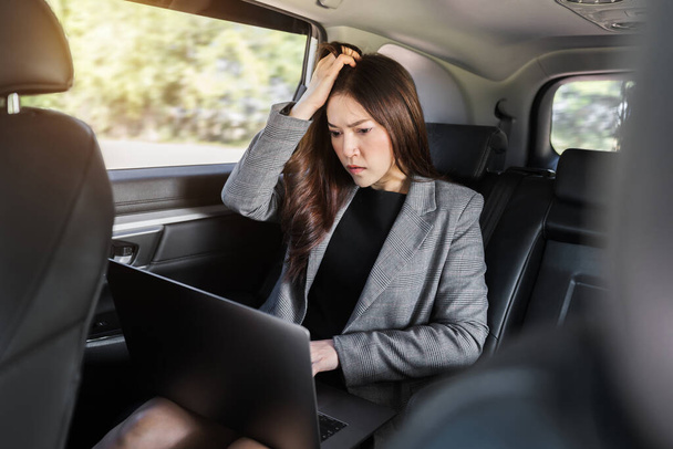 stressed young business woman using laptop computer while sitting in the back seat of car  - Photo, Image
