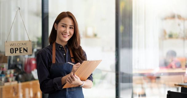 Porträt einer lächelnden asiatischen Unternehmerin, die hinter ihrem Café-Tresen mit offener Anzeigetafel steht - Foto, Bild
