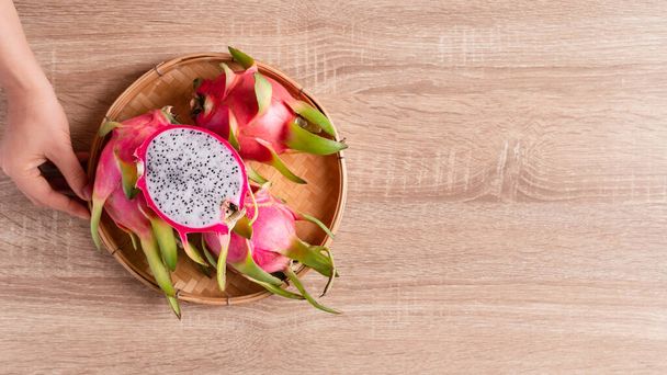 Dragon fruit or pitaya in a basket holding by woman hand on woden background, Tropical fruit, Table top view - Photo, Image