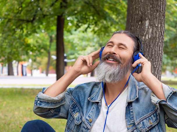 Muž středního věku vychutnává hudbu, když sedí na trávě v městském parku - svislá fotka. - Fotografie, Obrázek