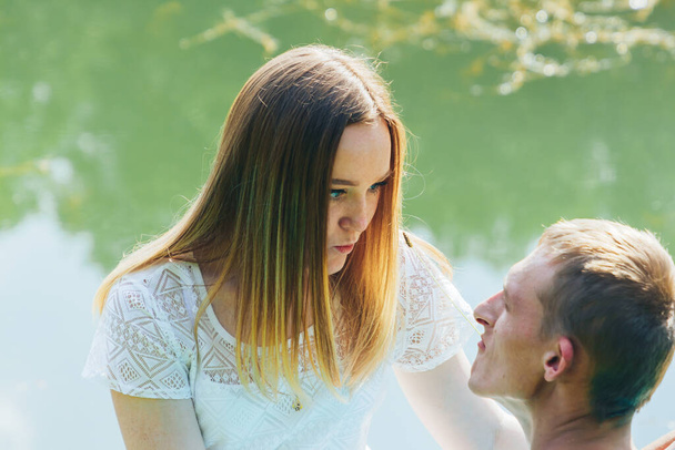 A couple in love is sitting by a lake in a park on a sunny day. Beautiful girl wants to kiss a young man - Fotoğraf, Görsel
