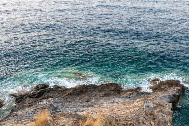 A beautiful view from a top of a rocky cliff on blue sea water waves on a  sunny day - Foto, Imagem