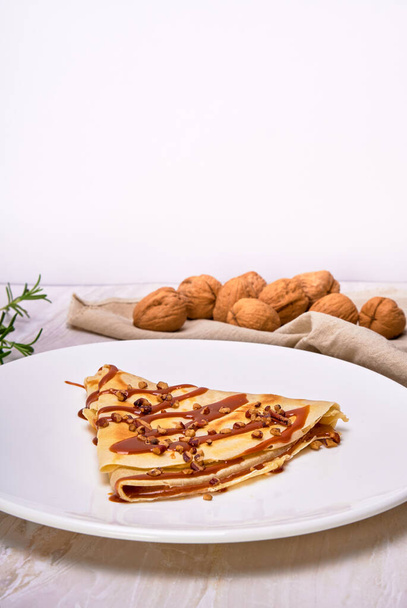 french crepes of cajeta (Dulce de leche) with walnuts on a white plate accompanied by walnuts on a brown cloth napkin. elegant concept. copy space for advertising. - Foto, Bild