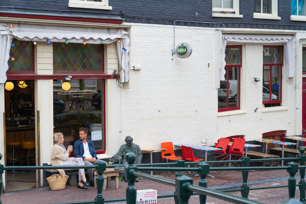 Amsterdam Netherlands - August 20 2017; Couple seated beside bronze statute outside Festina Lente cafe chatting and enjoying coffee on street. - Foto, Imagen
