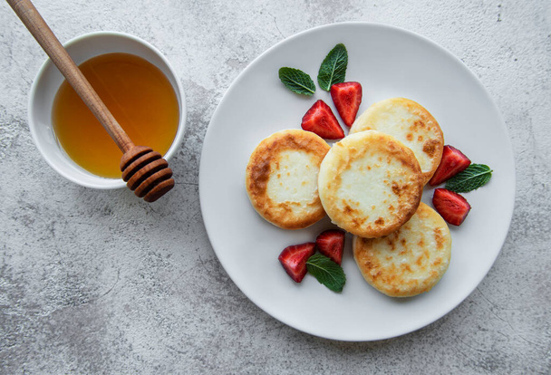 Τηγανίτες με τυρί, ρικότα σε κεραμικό πιάτο με φρέσκια φράουλα. Υγιές και νόστιμο πρωινό. Γκρι σκυρόδεμα. - Φωτογραφία, εικόνα