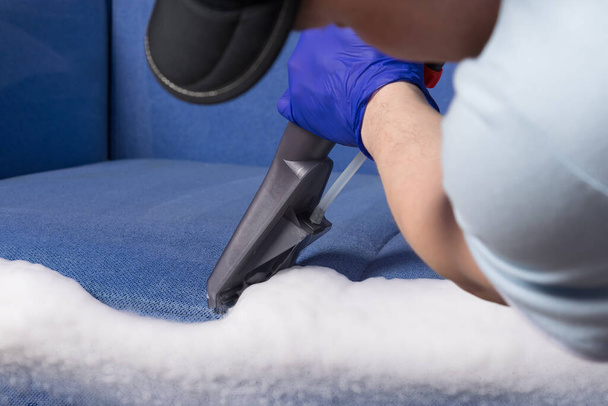in the hands of an employee of a cleaning company, the vacuum cleaner collects foam for dry cleaning of upholstered furniture - Fotografie, Obrázek