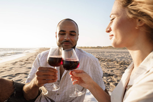 Portrait of a young couple sitting on the beach and drinking wine - Photo, image