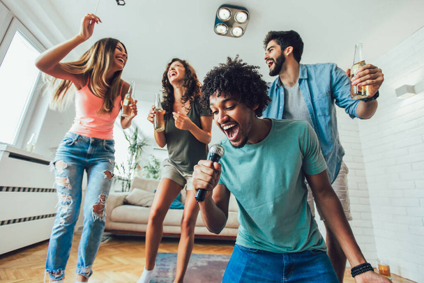 Grupo de amigos jugando karaoke en casa. Concepto sobre amistad, entretenimiento en el hogar y personas - Foto, imagen