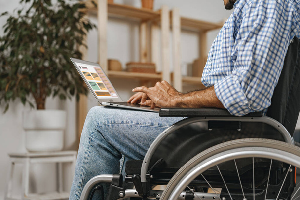 Disabled man sitting in a wheelchair and using laptop - Foto, Bild
