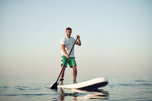 Young man in t-shirt and shorts floating on SUP board - Фото, зображення