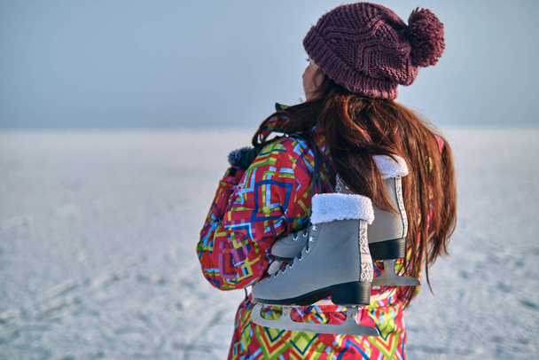 Una donna in tuta da sci tiene i pattini sulla spalla e guarda in lontananza, dopo aver sciato su un lago ghiacciato - Foto, immagini