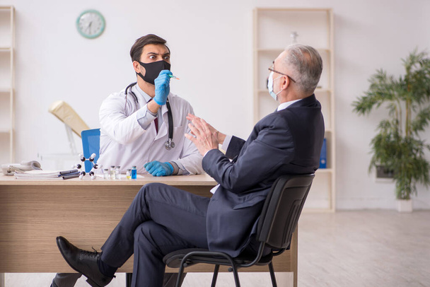 Old businessman visiting young male doctor in vaccination concep - Foto, afbeelding