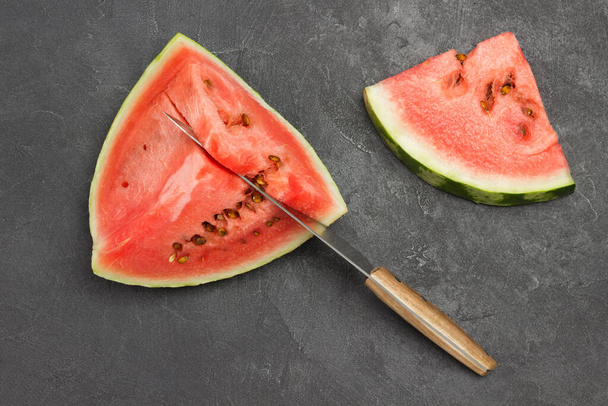 Knife in pulp of ripe watermelon. Slice of watermelon on table. Flat lay. Black background - Zdjęcie, obraz