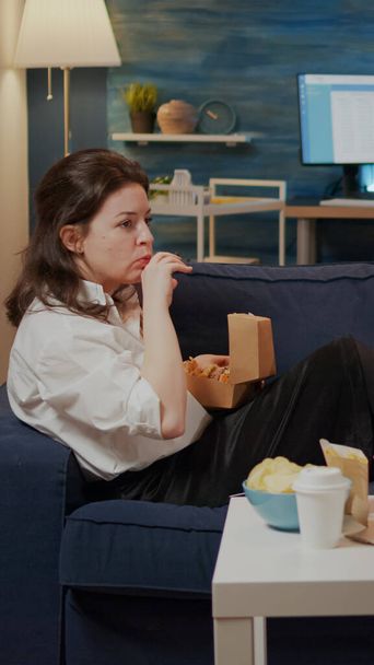 若い女性はハンバーガーを食べながらソファに寝そべって - 写真・画像