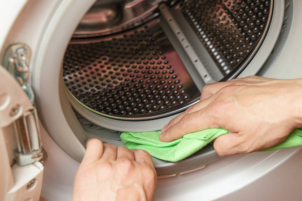 Ręce czyszczące wilgoć z bębna pralki. Koncepcja konserwacji pralki - Zdjęcie, obraz