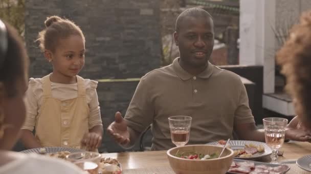 Waist-up of young Black man sitting at table, holding hands together with little daughter and cropped family members, praying before having dinner - Footage, Video