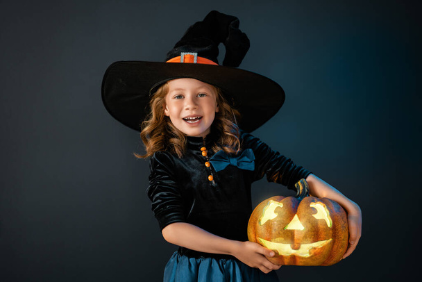 Happy Halloween! Cute little laughing girl in witch costume on black wall background.  - Zdjęcie, obraz