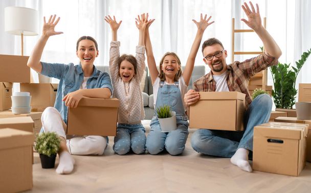 Happy young family are moving to new apartment. Parents and daughters with boxes. - Fotoğraf, Görsel