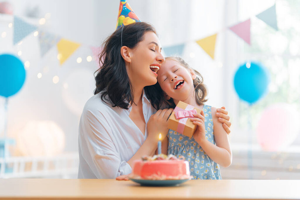 The kid is blowing out the candles on the cake. Mother and daughter are celebrating birthday. - Foto, Imagen