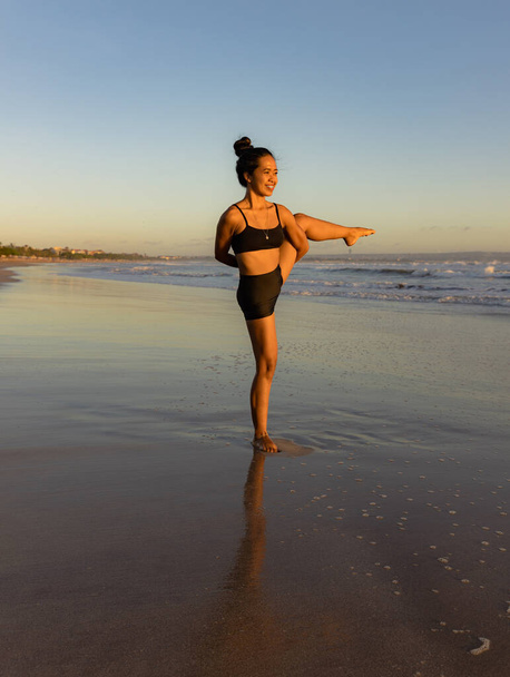 Beach yoga practice. Svarga Dvijasana, Paradise Bird Pose. Strong legs. Standing balancing asana. Healthy lifestyle. Fit body. Copy space. Seminyak beach, Bali Indonesia - Фото, изображение