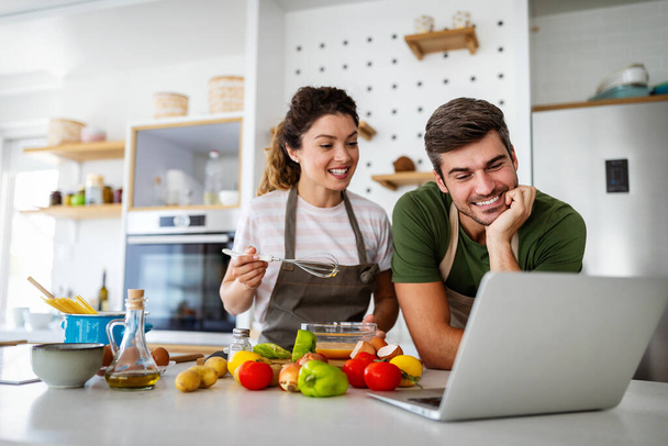 Happy young couple preparing food in kitchen at home. Healthy food, people concept - Foto, Imagem