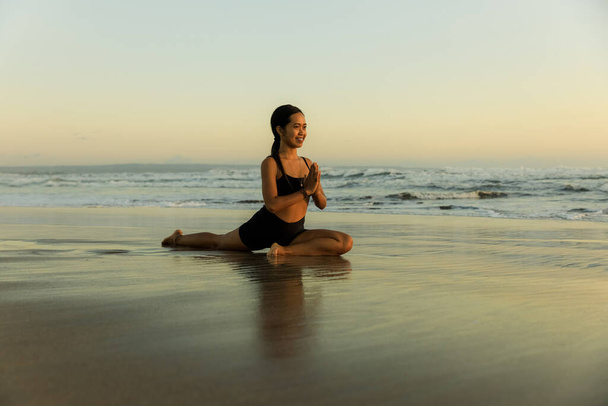 Yoga en la playa. Mujer delgada practicando Ardha Kapotasana, Media Paloma Pose. Manos en namaste mudra. Abridor de pecho mejorando la respiración. Estilo de vida saludable. Retiro de yoga. Hora del atardecer. Playa de Seminyak Bali - Foto, imagen