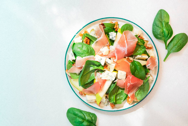 Pear salad with prosciutto, blue cheese, spinach, walnuts on white background, top view, copy space - Foto, Bild