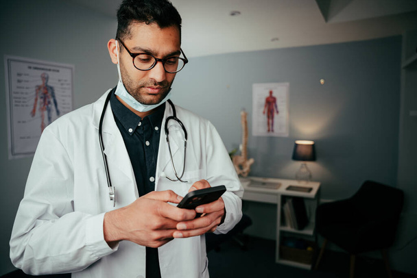 診療所に立っている携帯電話のデバイス上の混合レース男性看護師テキスト - 写真・画像