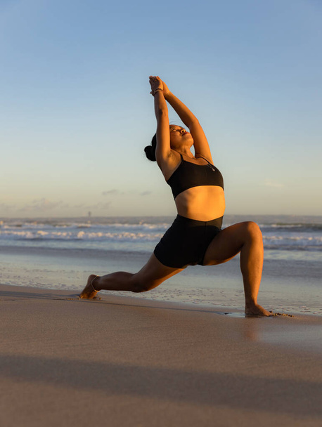 Sonnenuntergang Strand Yoga. Anjaneyasana, Low Lunge Pose. Mondsichel-Pose. Zurücklehnen und Asana beugen. Stützende Muskeln. Flexible Wirbelsäule und Rücken. Yoga-Retreat. Seminyak Strand, Bali, Indonesien - Foto, Bild