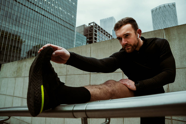 Caucasian male athlete stretching calves while running through city training for race - Foto, Bild