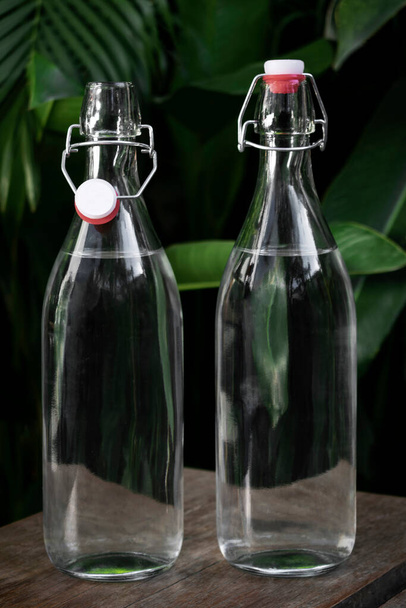 Bahçe masasının üzerinde açık beyaz cam kaplama su şişesi. - Fotoğraf, Görsel