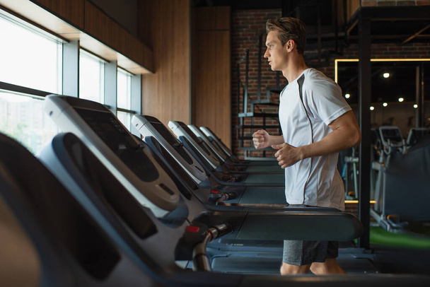 Seitenansicht des Sportlers, der im Fitnessstudio auf dem Laufband läuft - Foto, Bild