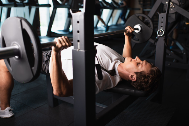athletic man working out on weightlifting exercising machine in gym - Photo, Image