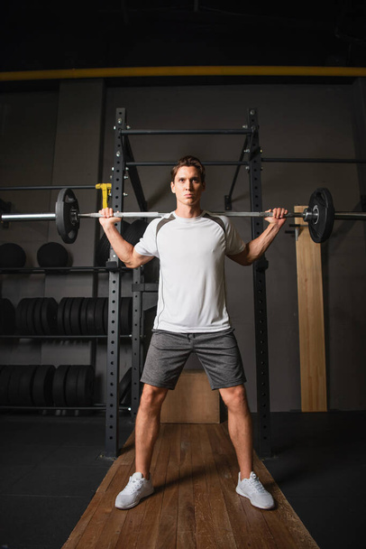 vista completa del hombre en entrenamiento de ropa deportiva con barra de pesas en el gimnasio - Foto, Imagen